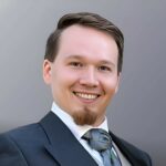 Porträt von Robert Skawinski, ein lächelnder Mann im Anzug mit Krawatte vor neutralem Hintergrund.