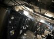 Ein altes, staubiges Rechenzentrum mit dunklen Serverracks, herabhängenden Kabeln und schwachem Licht, das durch ein Fenster fällt.