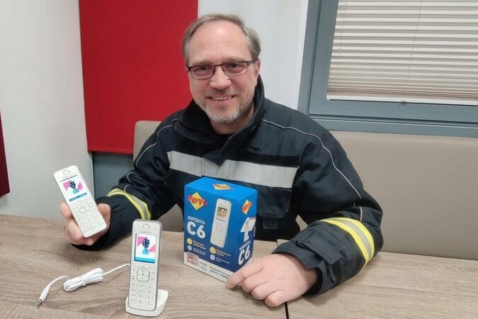 DECT Feuerwehr Eichgraben: Kommandant HBI Andreas Buchschachner präsentiert zwei FRITZ!Fon C6 Telefone mit Feuerwehr-Logo auf dem Display und Originalverpackung – installiert von SKAWINSKI GmbH