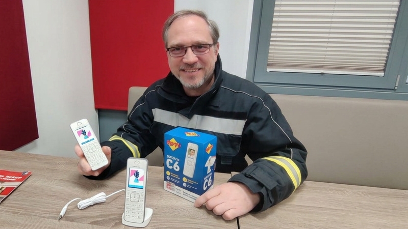 DECT Feuerwehr Eichgraben: Kommandant HBI Andreas Buchschachner präsentiert zwei FRITZ!Fon C6 Telefone mit Feuerwehr-Logo auf dem Display und Originalverpackung – installiert von SKAWINSKI GmbH